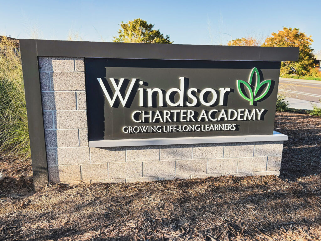 Monument sign for Windsor Charter Academy with raised lettering and a green leaf logo.