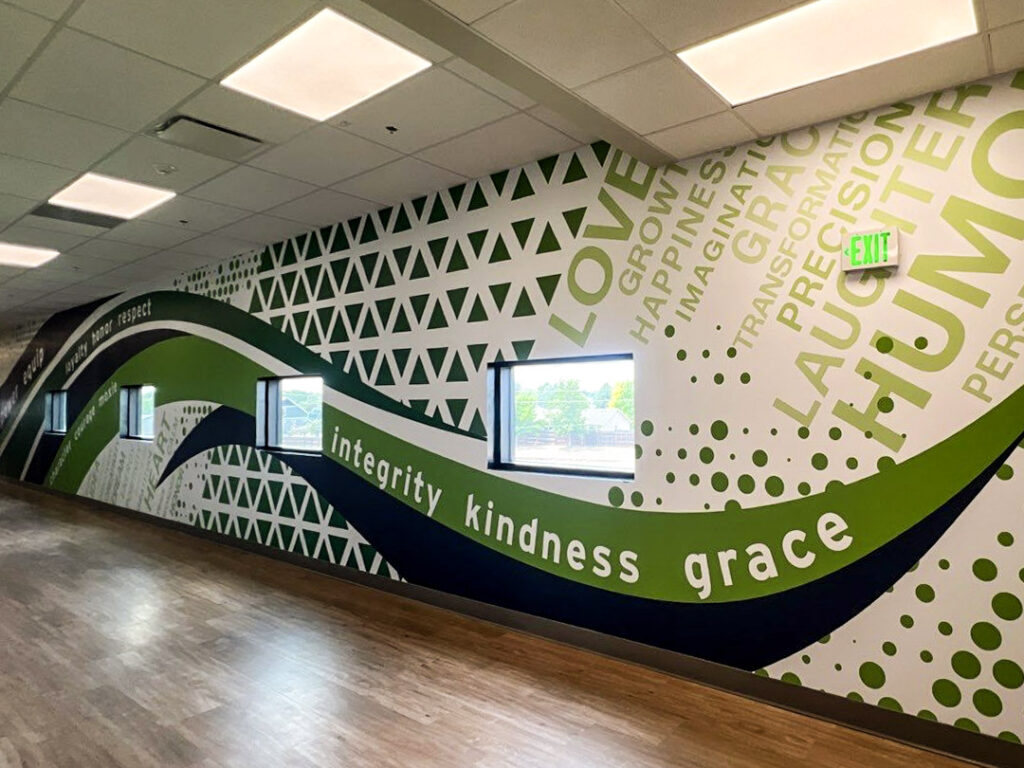 Colorful vinyl wall mural at Windsor Charter Academy featuring sweeping green and navy shapes with words like integrity, kindness, grace, love, and imagination.