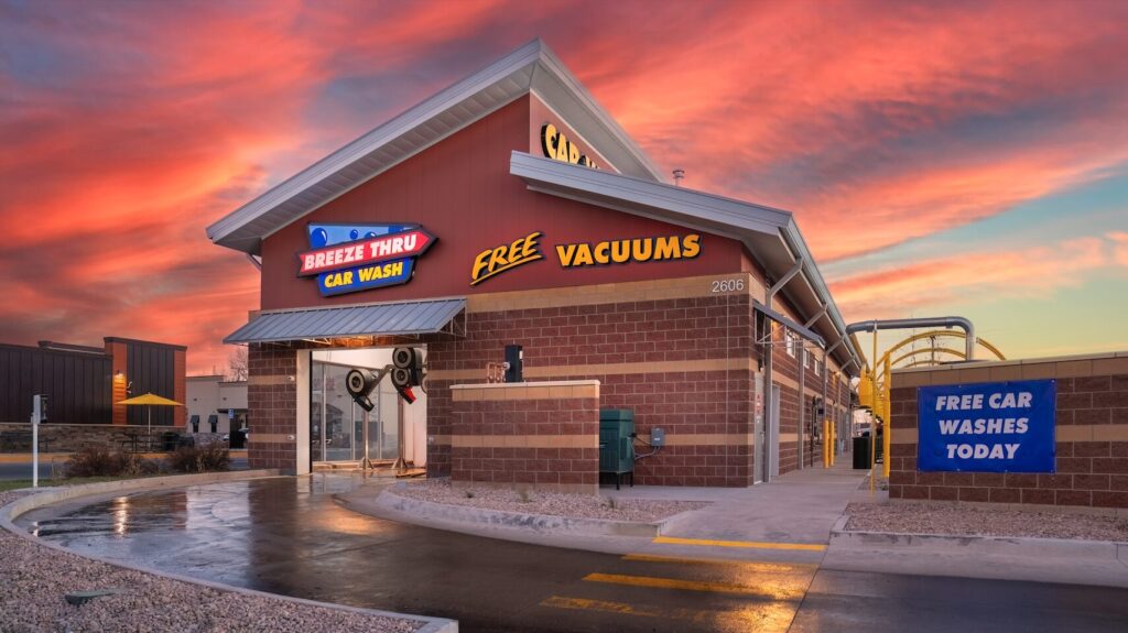 A front-facing view of Breeze Thru Car Wash in Laramie, WY at dusk, showing illuminated channel letters, accent lighting, and the car wash entrance beneath a vivid sunset sky.
shine