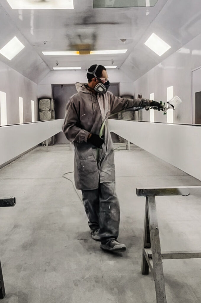 Fabrication worker wearing protective gear spray-painting a sign component