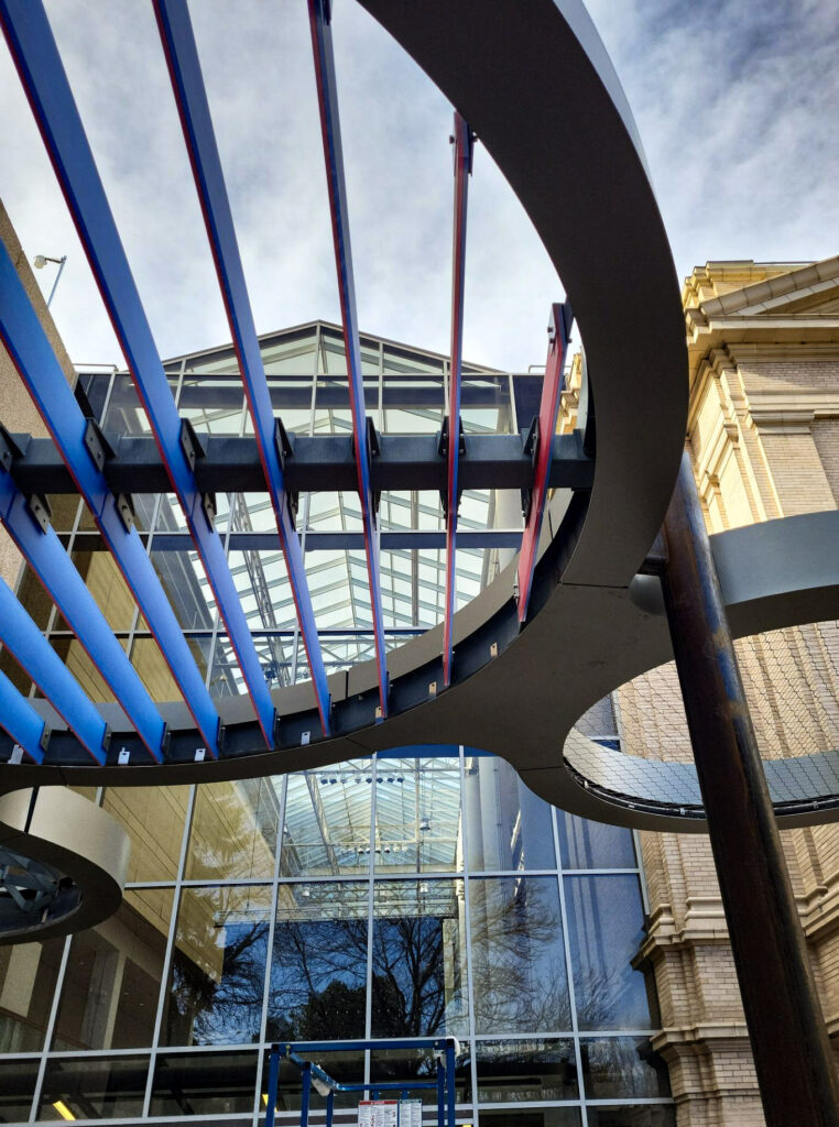 Upward view of curved metal canopy with red and blue beams at the Denver Museum of Nature & Science entrance.