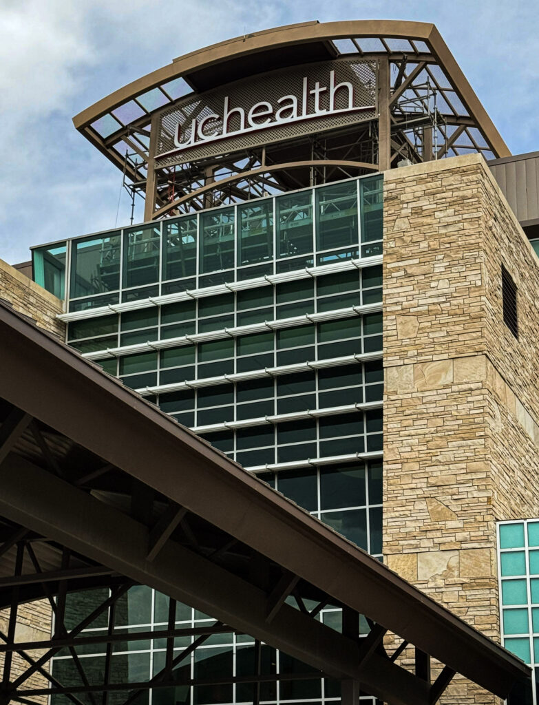 Exterior view of a sign project for UCHealth Medical Center of the Rockies in Loveland, Colorado, with glass façade, stone tower, and rooftop UCHealth signage.