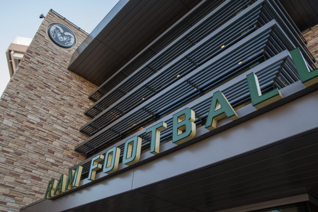 Colorado State University Rams Football signage mounted on the exterior of a modern stadium building with stone and metal architectural features.