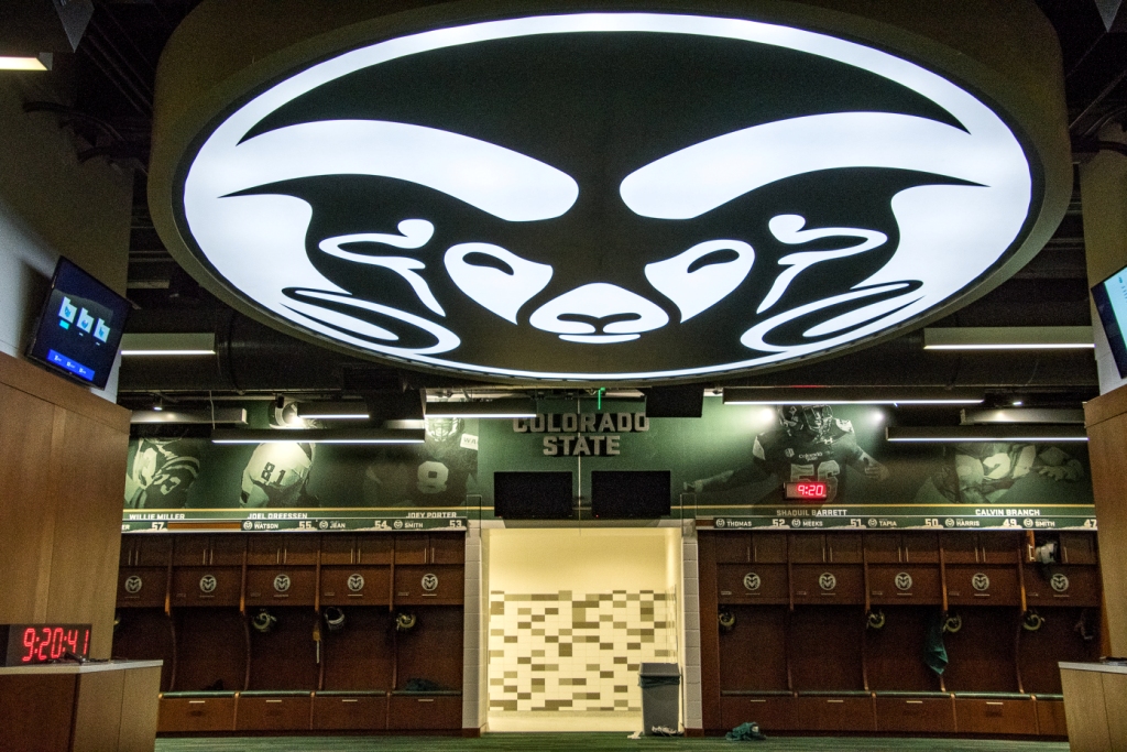 Interior of the Colorado State University football locker room featuring branded graphics, illuminated ceiling signage, and team lockers.